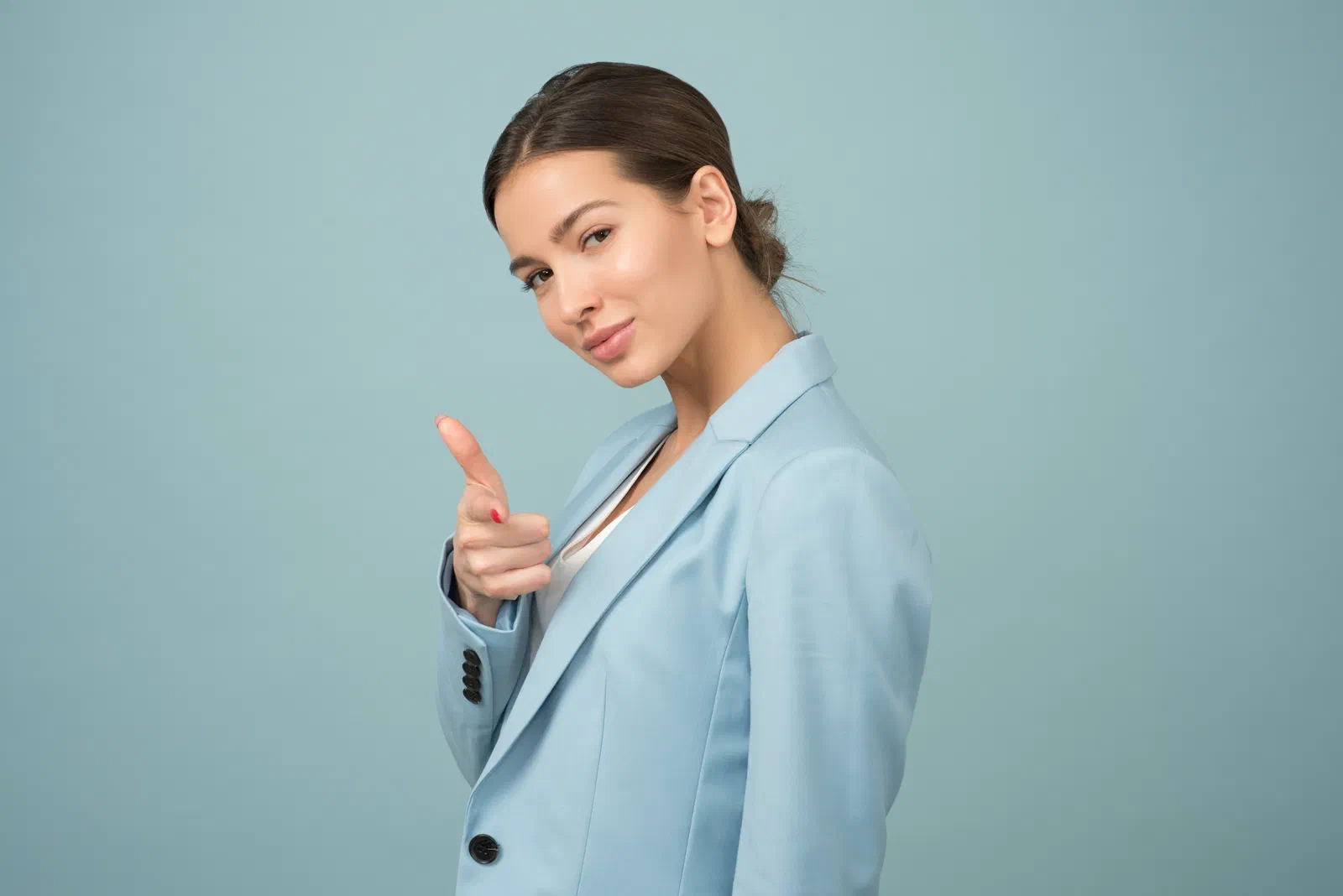 A confident woman in a light blue blazer smiling and pointing toward the camera