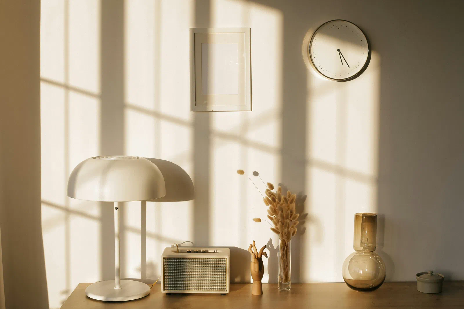 A calm, sunlit room with a lamp, a vase and a wall clock on a wooden table