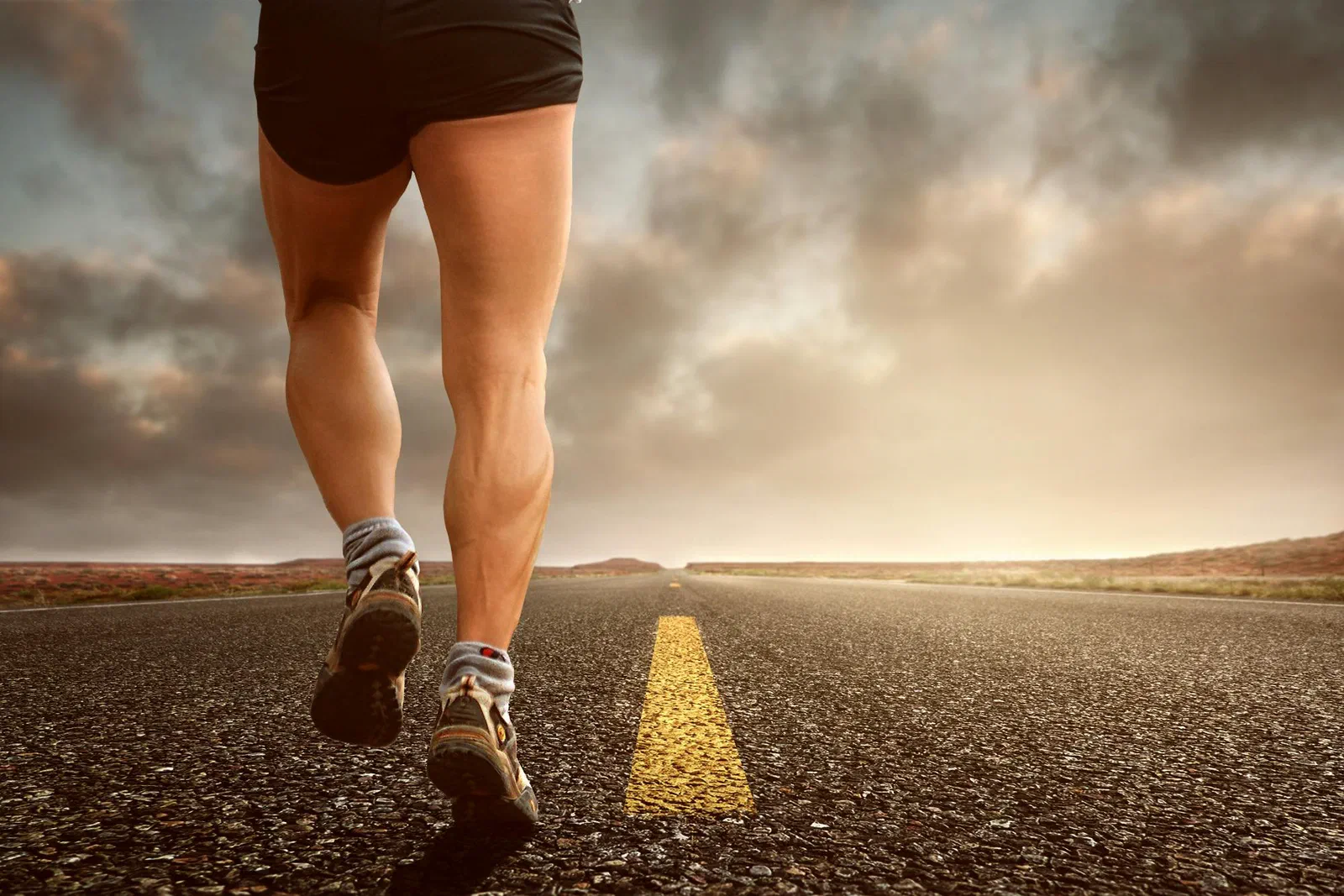 Close-up of a runner’s legs mid-stride on an open road under a dramatic sky