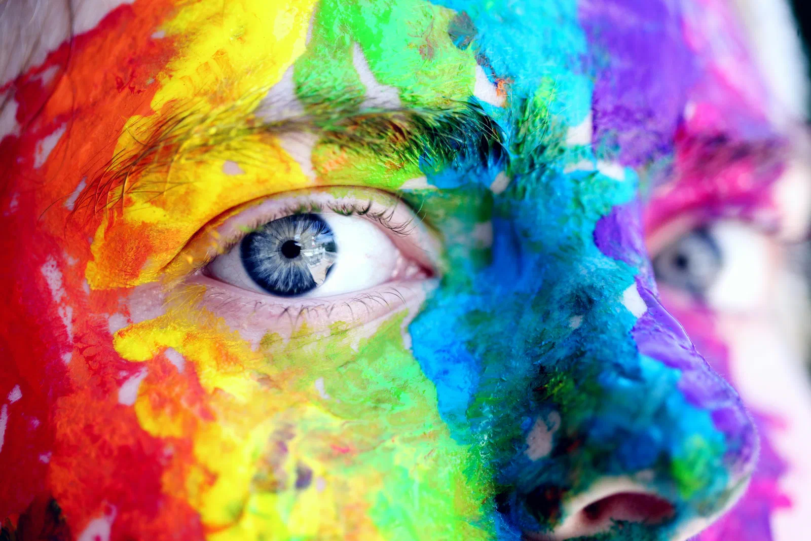 Close-up of a person’s eye with the face painted in rainbow colors
