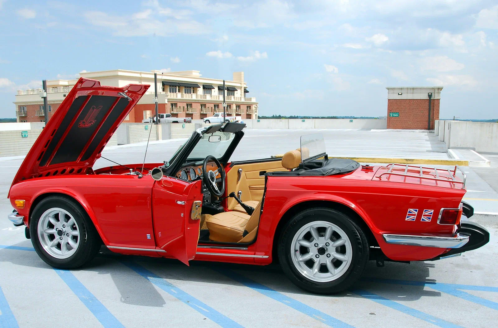 A red vintage convertible sports car with its hood and door open on a parking deck