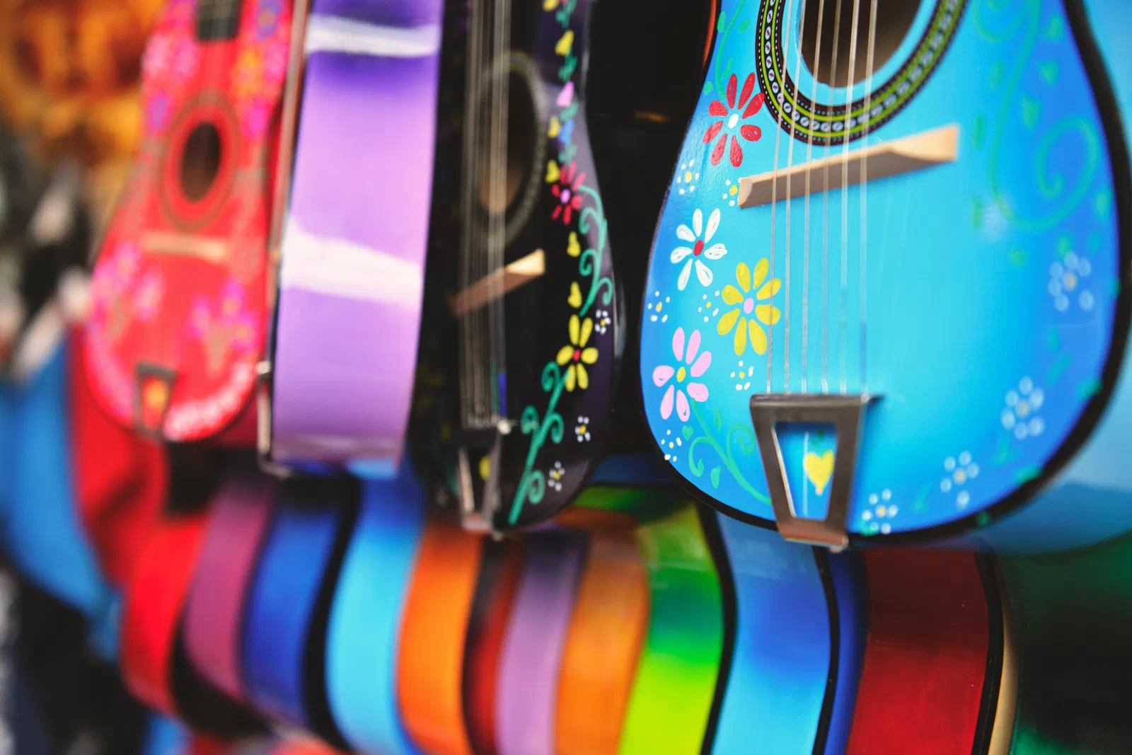Brightly painted guitars and ukuleles in many colors hanging side by side