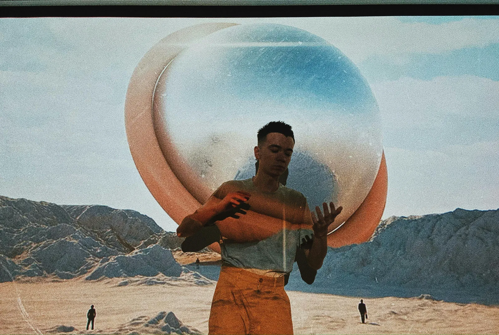 A man standing in a desert holding a large glass sphere above his head