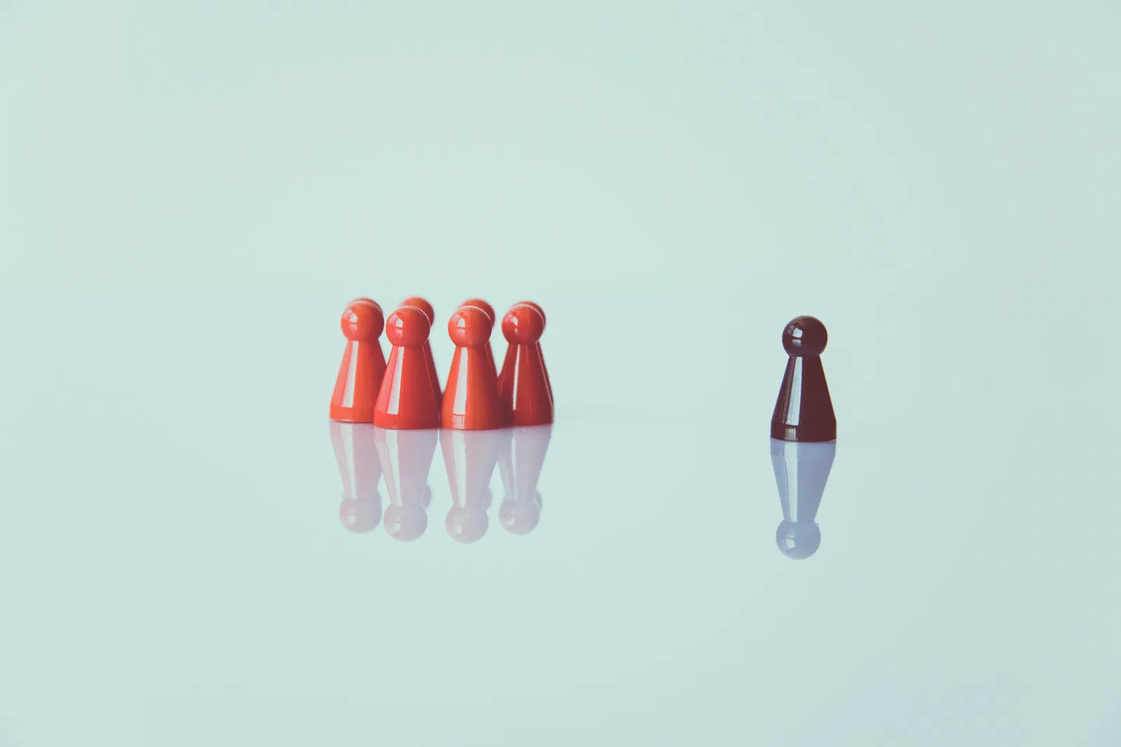 A group of red game pieces standing together, facing a single dark piece standing apart