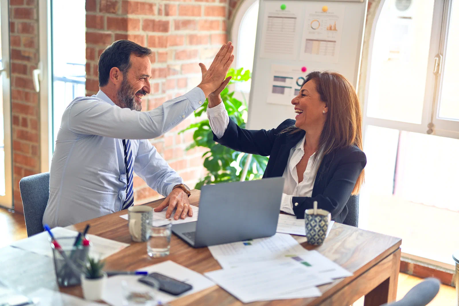 A man and a woman giving each other a high five across a desk in a bright office